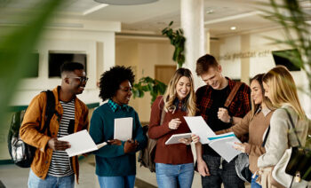 Happy female student showing test results to her friends while standing in a lobby.